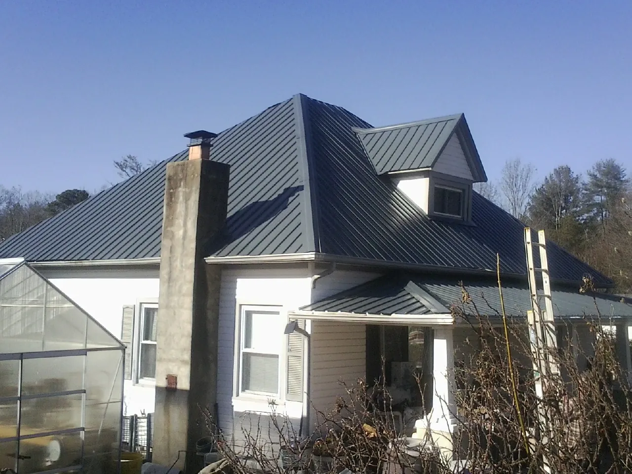 Dark blue standing seam metal roof on a white farmhouse with dormer — Slate & Tile Roof Repair by Roofing Brothers in Tucker