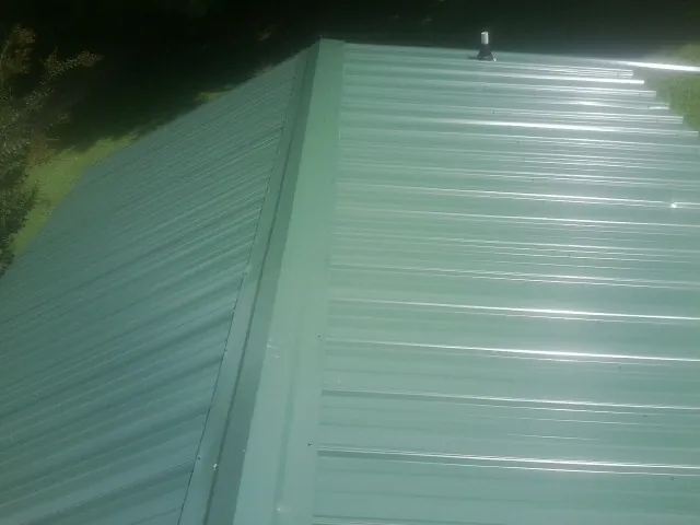 New green metal panels meeting at the ridge of a roof — Flat Roof Repair work by our crew in Tucker