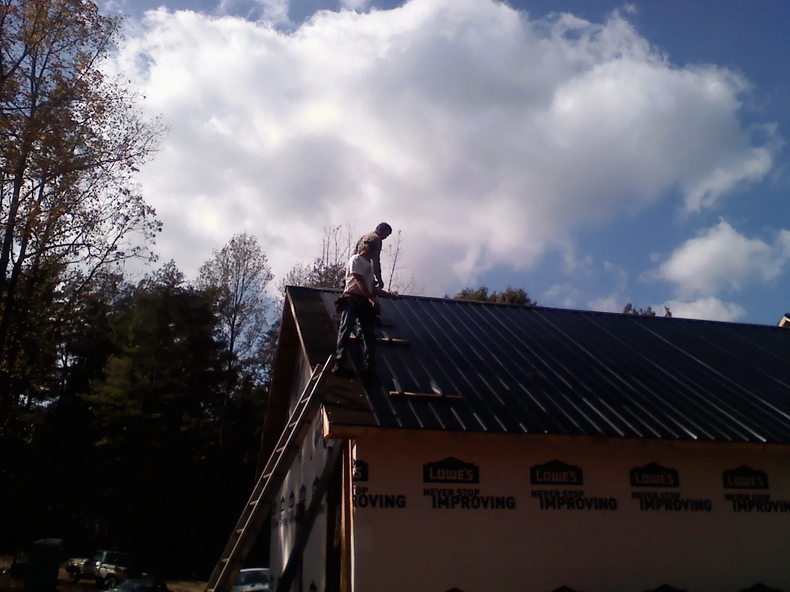 Roofer fastening dark metal panels high against a cloudy sky, from a Roof Inspection job in Tucker