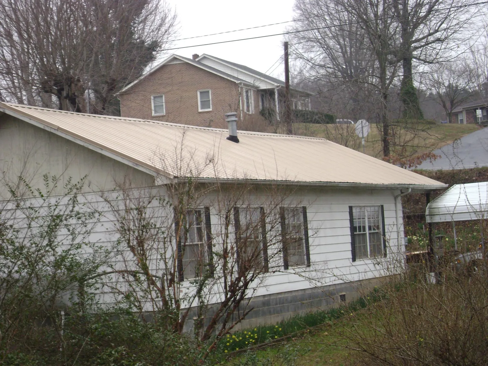 Tan metal roof on a white sided house set into a hillside — Commercial Roofing by Roofing Brothers in Tucker